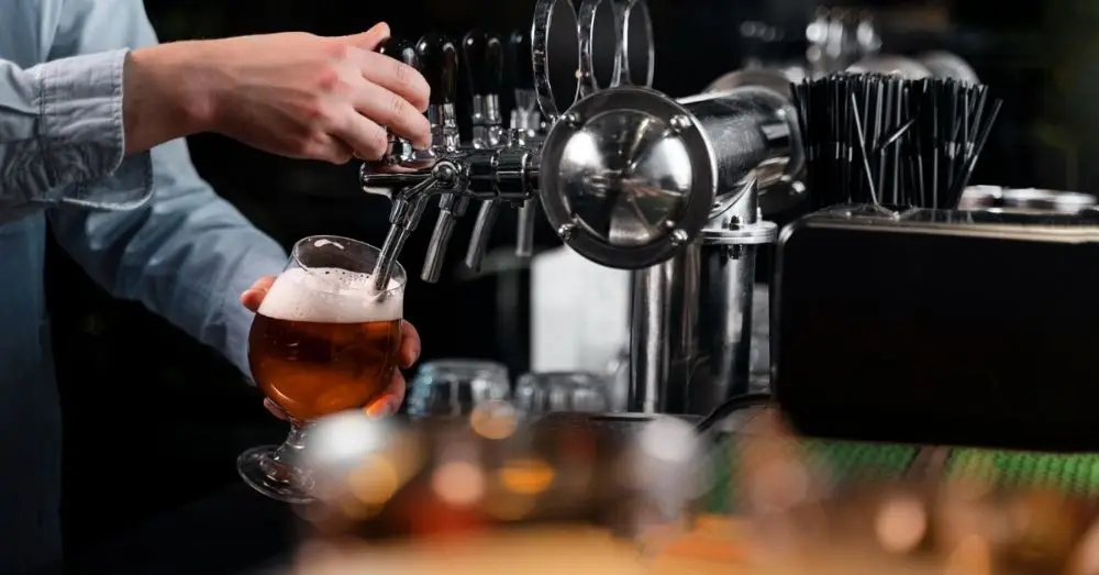 Bartender pouring an amber draft beer into a glass from a tap on a shiny chrome tower.