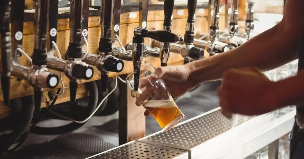 Bartender pouring a glass of draft beer from a tap.