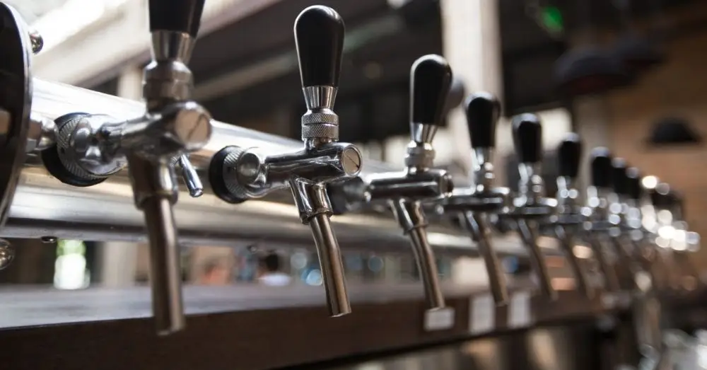 A close-up row of shiny, chrome draft beer taps with black handles on a bar.