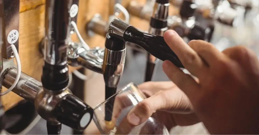 Close-up of a hand pulling a draft beer handle to pour into a glass, with other beer taps visible.