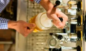 Hands pouring draft beer from a tap into a glass mug at a bar counter