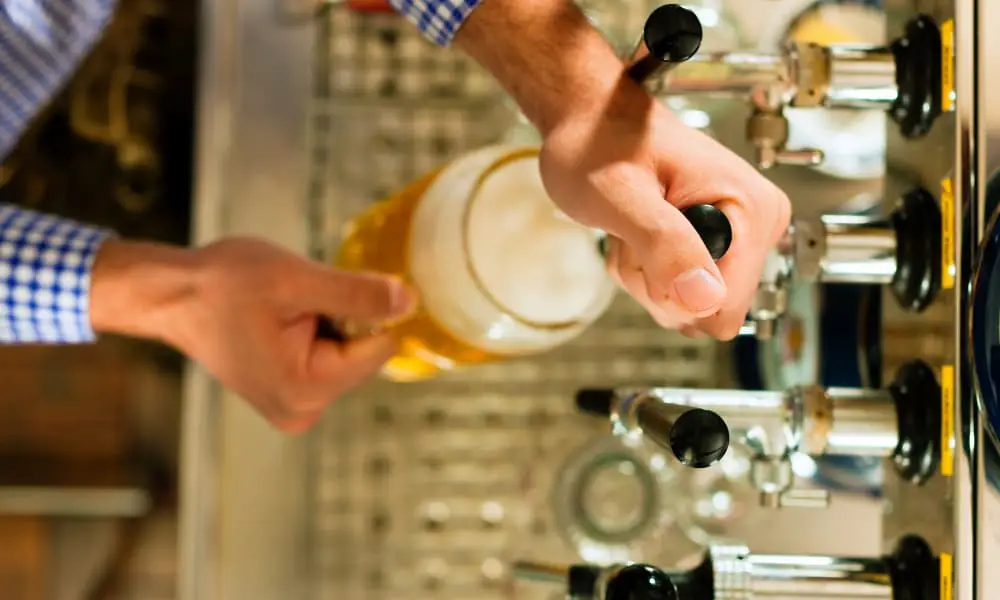 Hands pouring draft beer from a tap into a glass mug at a bar counter