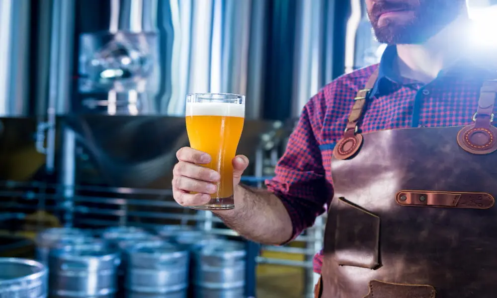 Brewer holding a glass of beer in a brewery.