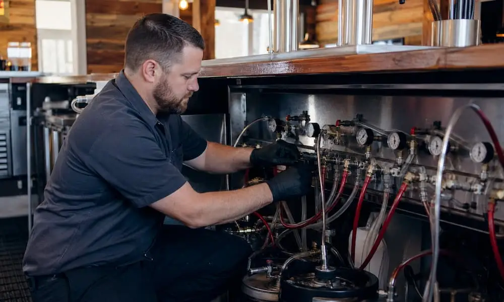 Technician repairing a draft beer system under a bar counter