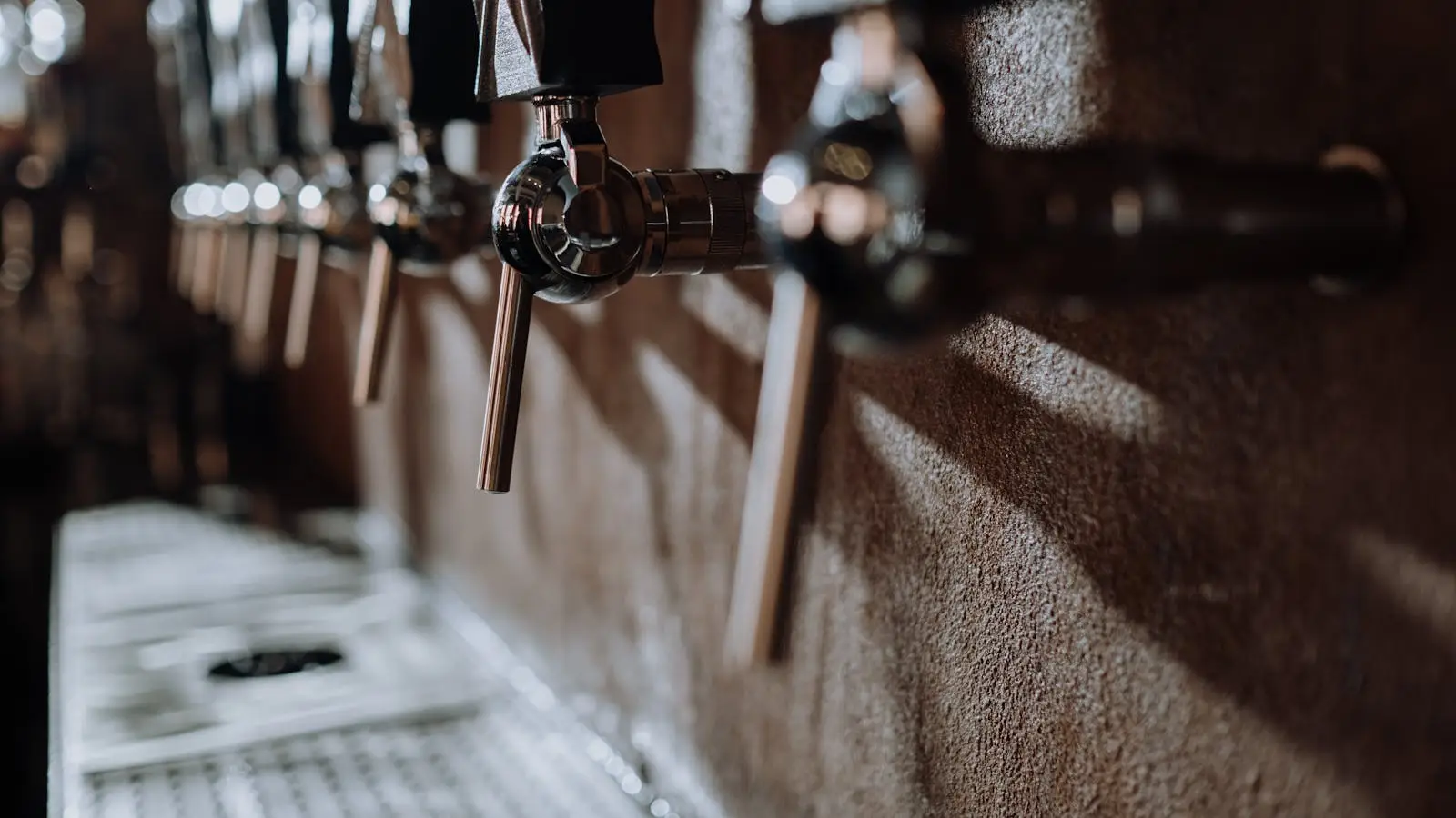 Close-up of beer taps in a bar with warm lighting and texture, representing clean draft beer systems.