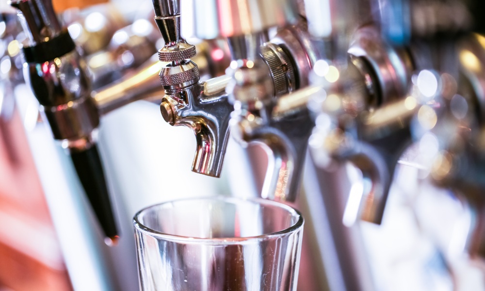A close-up of an empty glass sitting directly beneath a row of polished chrome beer taps