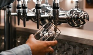 A person holding a clear glass under a shiny chrome beer tap that is slow or not pouring