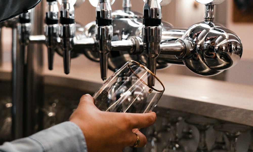 A person holding a clear glass under a shiny chrome beer tap that is slow or not pouring