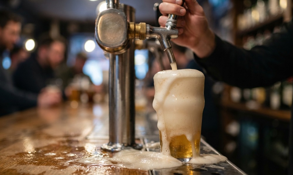 a bartender's hand pulling a draft beer tap, filling a glass to the brim with overflowing foam