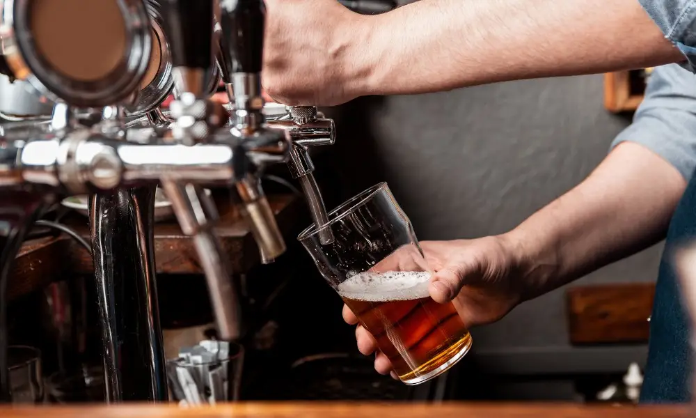A bartender pours an amber draft beer from a chrome tap handle
