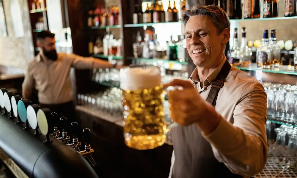 bartender holding out a large dimpled glass mug filled with frothy beer