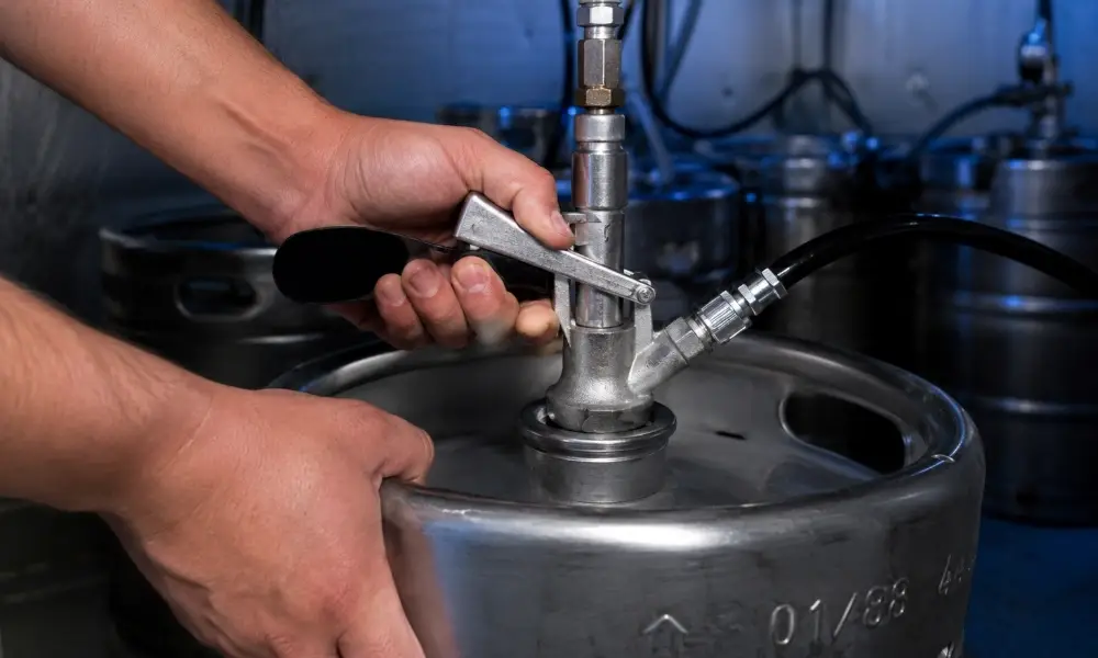 A close-up of hands properly seating a D-system coupler onto a keg valve in a commercial cooler.