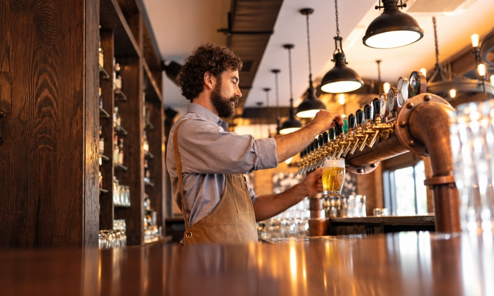 bartender with curly hair reaches toward a long row of beer tap handles
