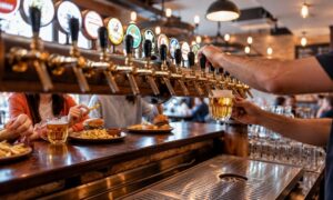 pours a glass of draft beer from a long row of brass taps