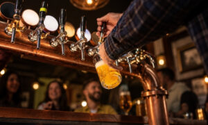 bartender's hand pulling a copper tap handle to pour a glass of light beer