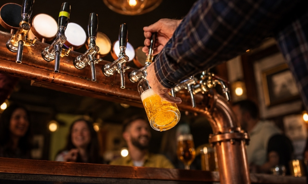 bartender's hand pulling a copper tap handle to pour a glass of light beer